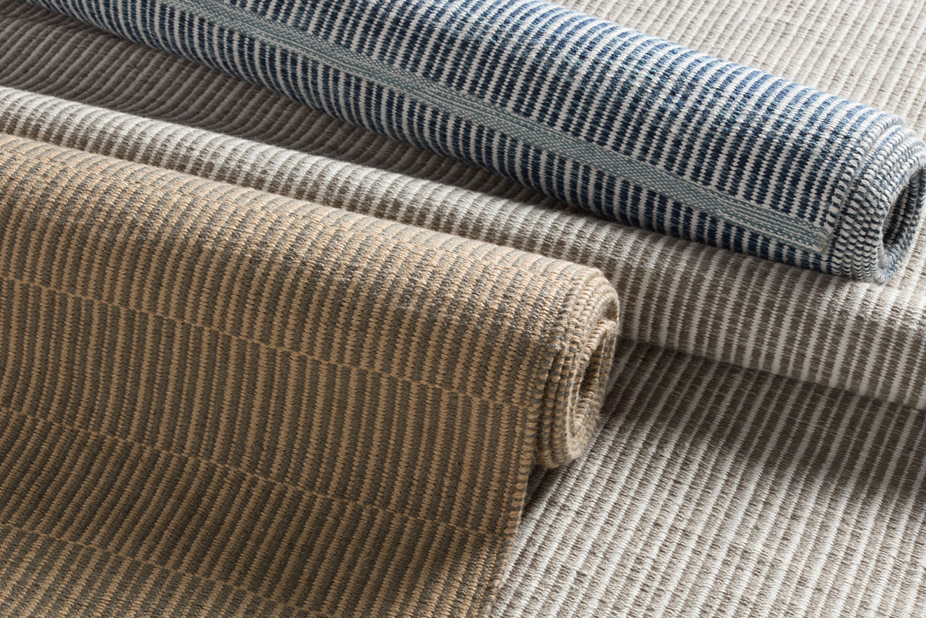 Rolled neutral and striped outdoor rugs in tan, gray, and blue shades