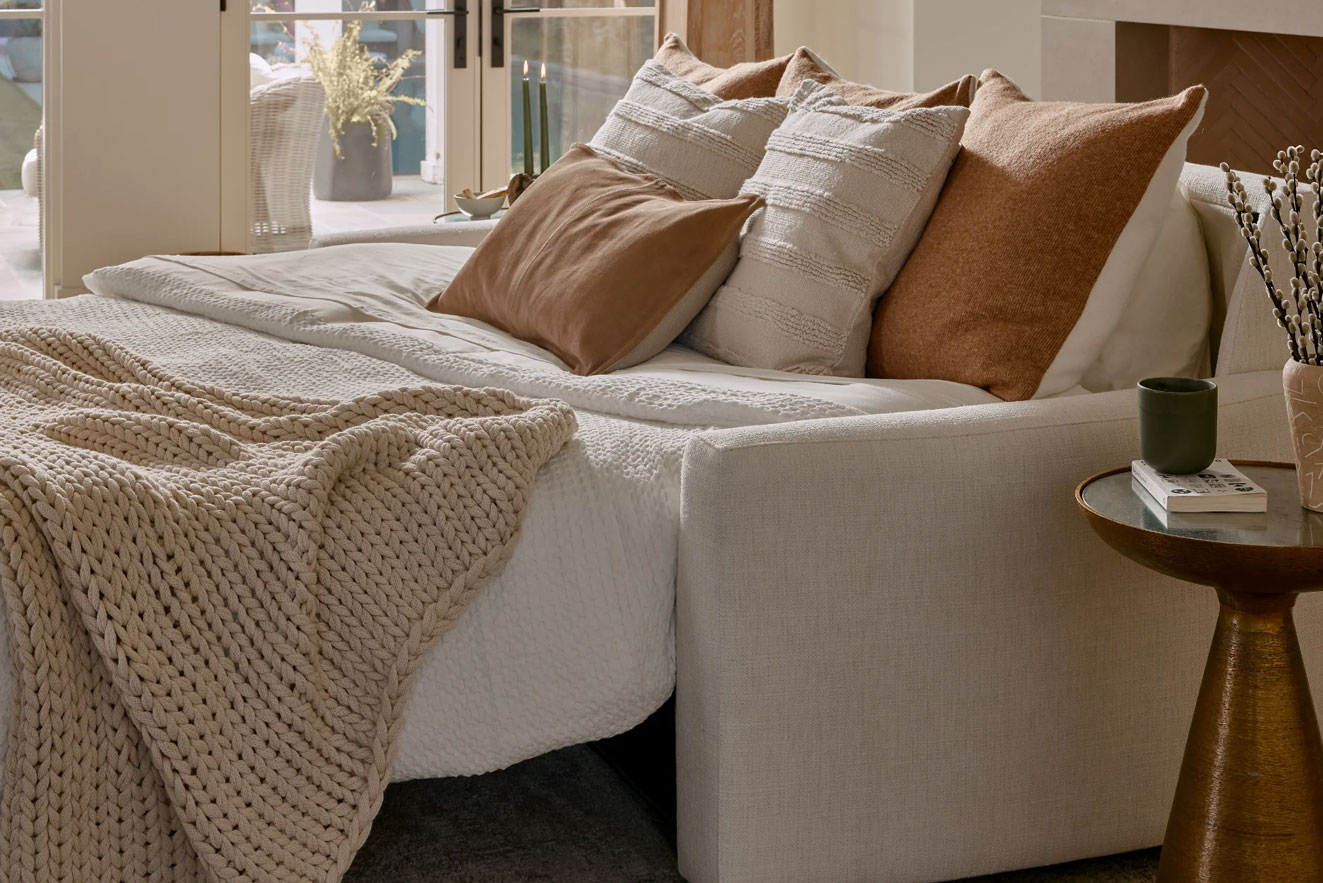Close-up view of an American Leather sleeper sofa open as a bed, showing a comfortable mattress, pillows, and cozy blankets.