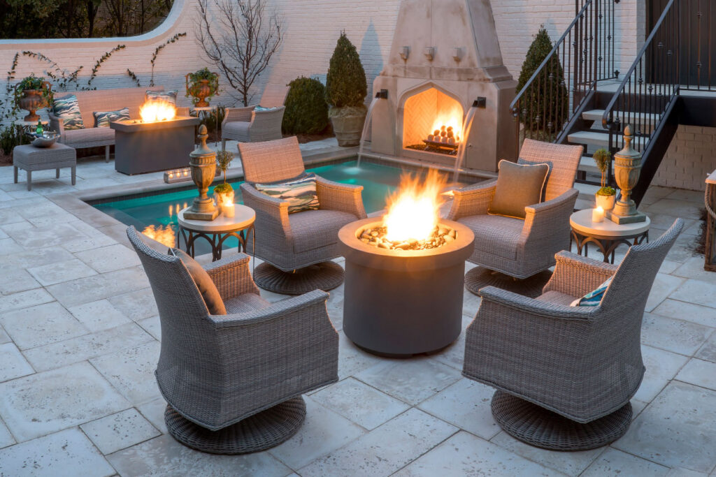 Luxury patio decor with round fire table, wicker chairs, pool, and outdoor fireplace creating elegant winter outdoor space