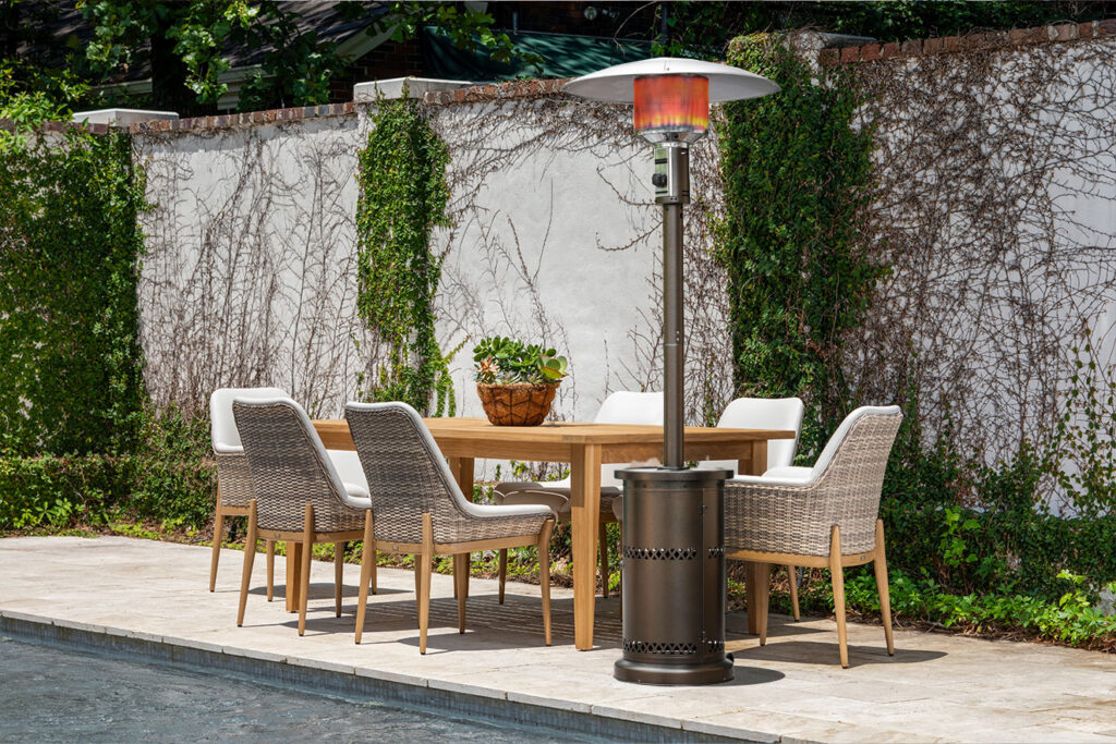 Patio decor featuring teak dining table with wicker chairs and freestanding outdoor heater for comfortable year-round dining