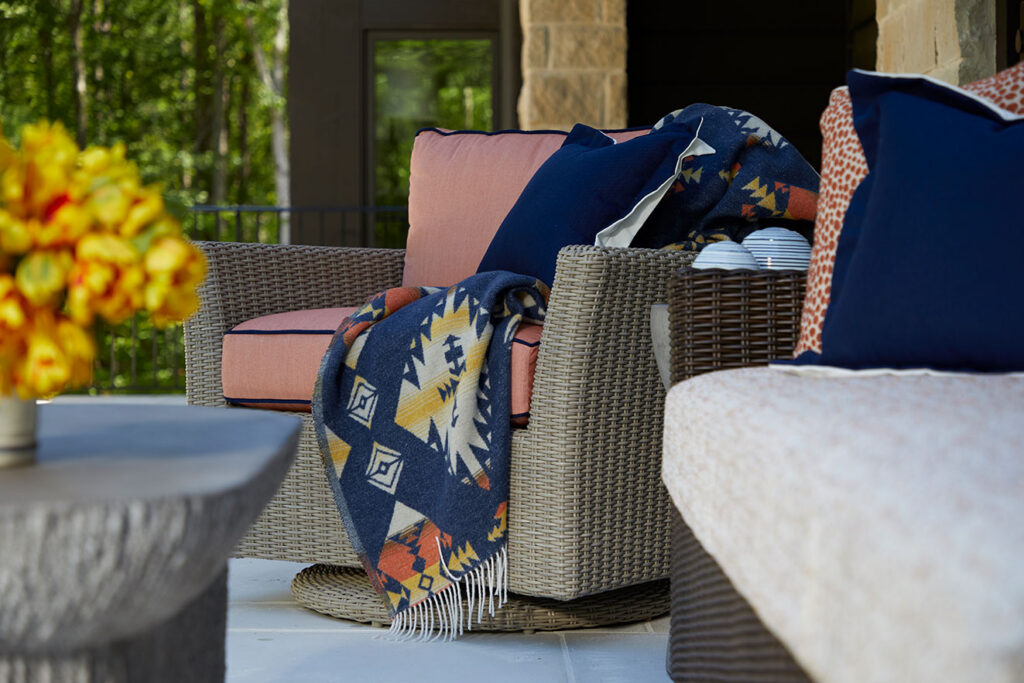 Outdoor wicker swivel chairs with cushioned seating and patterned throw pillows on a covered patio