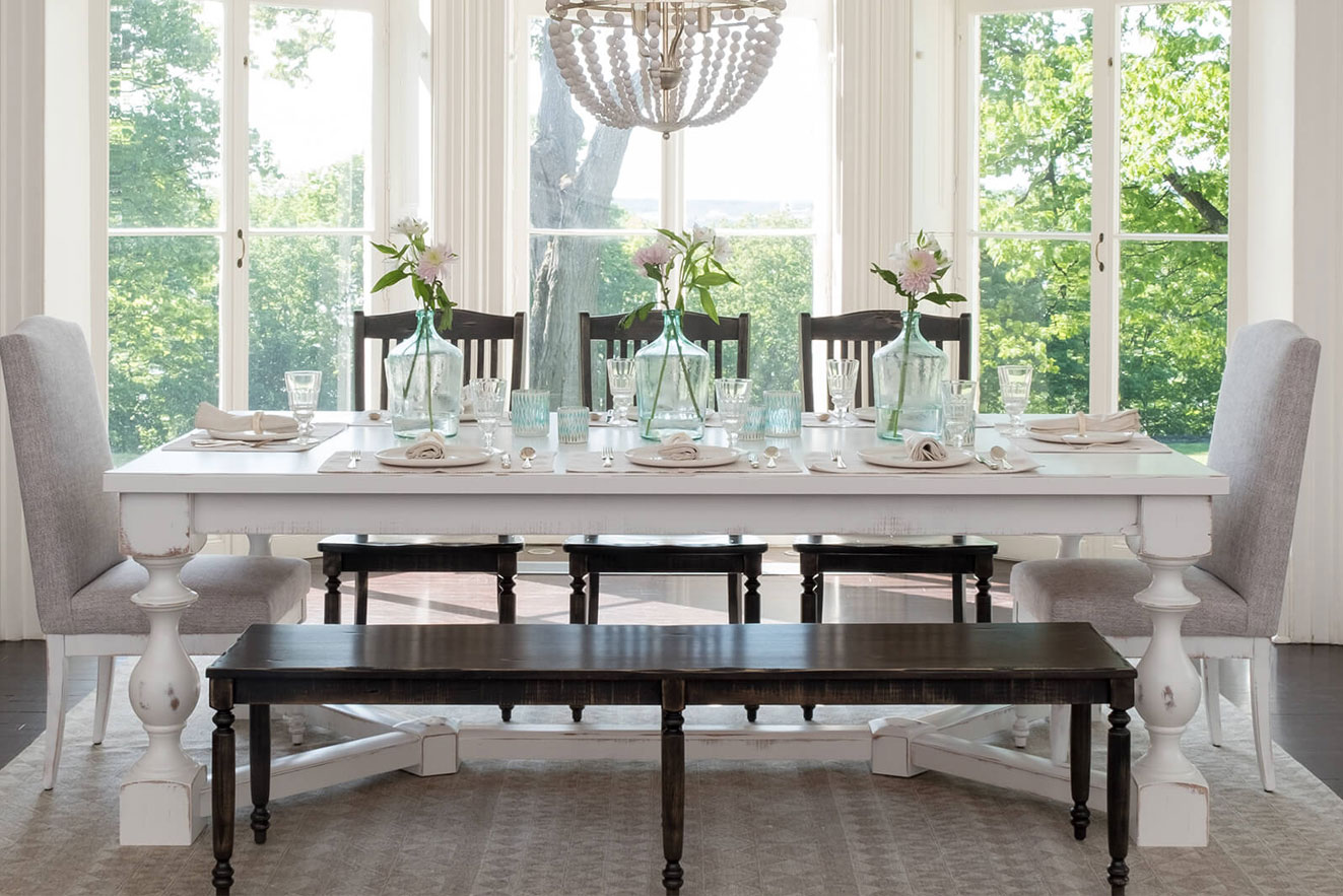 Custom two-tone dining set featuring a white distressed farmhouse table and a dark wood bench in a bright sunlit room.