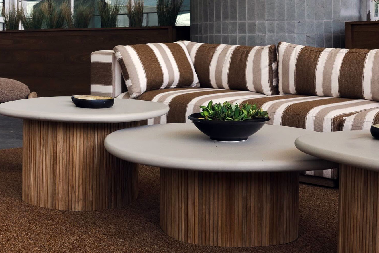 Modern outdoor patio setup at Fowler Brothers Co featuring round fluted wood base coffee tables with stone tops and a brown and white striped outdoor sectional sofa.