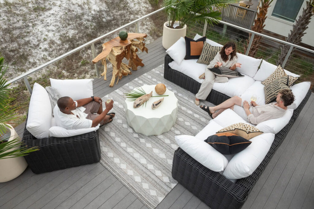 Friends relaxing on a styled outdoor deck with dark wicker deep seating, white performance cushions, a patterned outdoor rug, and accent pillows from Fowler Brothers Co. Home and Patio in Chattanooga Tennessee