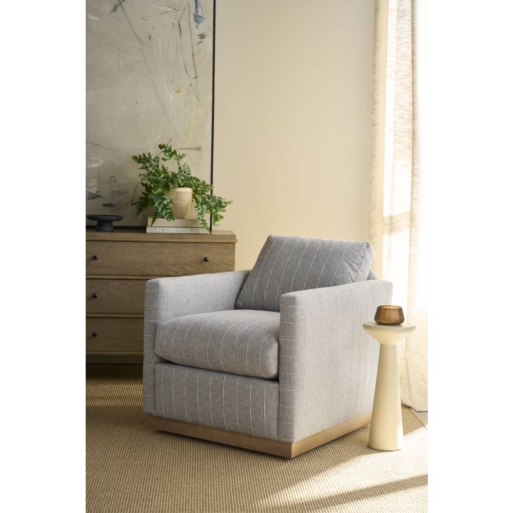Gray upholstered swivel accent chair with wood base in a cozy living room setting