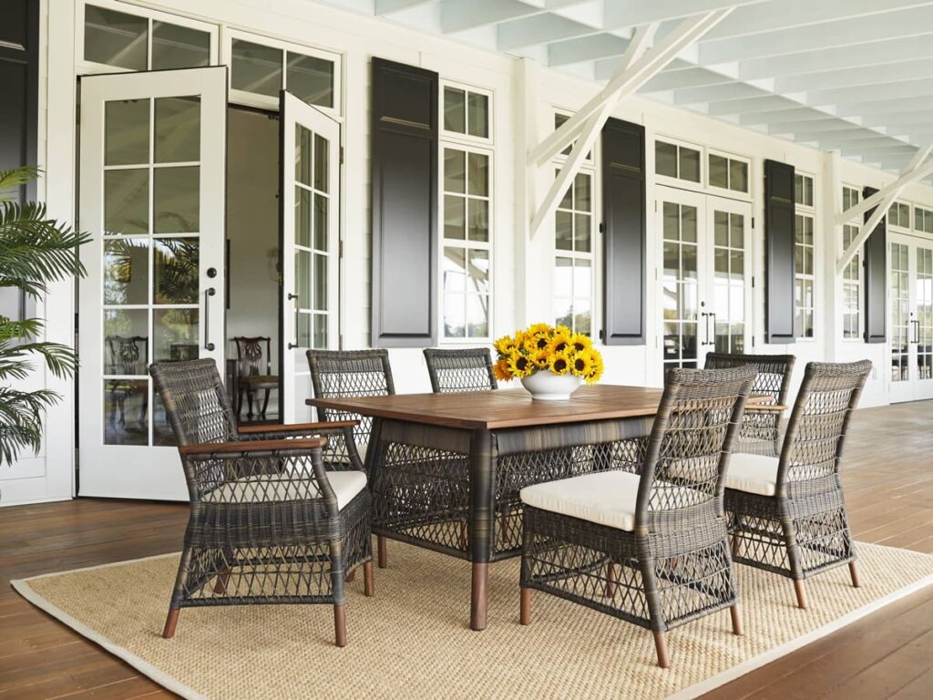 Fall outdoor dining set with woven wicker chairs and a wood top table on a covered porch