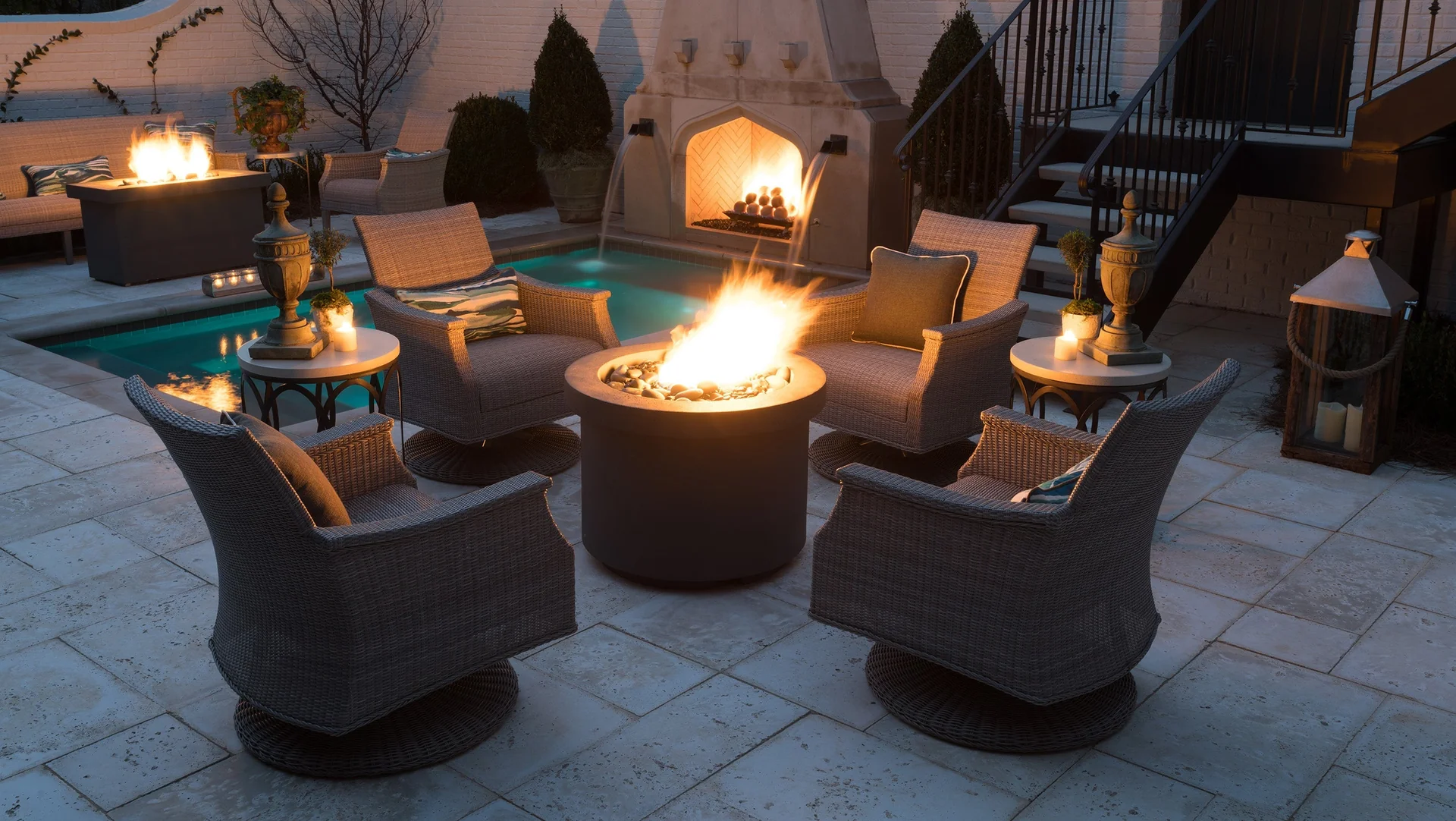 Outdoor fire pit surrounded by woven swivel chairs on a patio at dusk