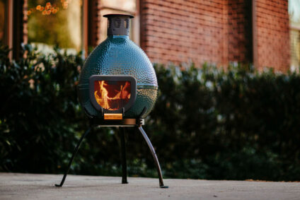 Big Green Egg Chimenea with a burning fire, placed on an outdoor patio, providing warmth and ambiance for backyard gatherings