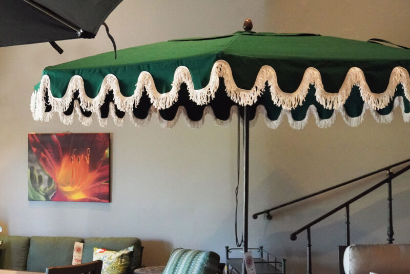 Elegant green fringe umbrellas displayed in an outdoor furniture showroom with cozy seating.