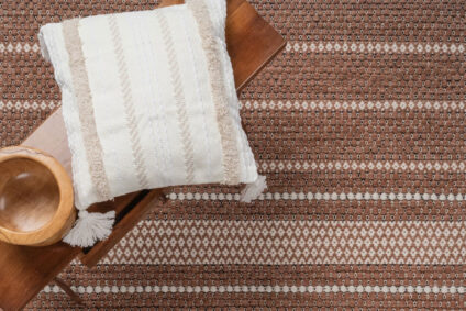 Woven brown and ivory outdoor rug styled with neutral pillow and wooden accents